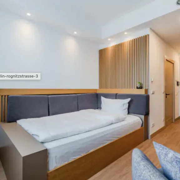 Modernes, helles Hotelzimmer mit Einzelbett, Holzboden und minimalistischer Einrichtung.