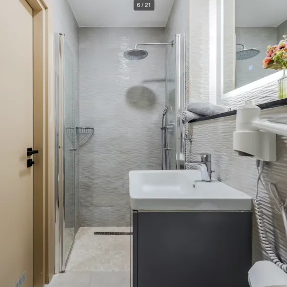 Modernes, schmales Badezimmer mit Dusche, Waschbecken, Spiegel und Föhn an der Wand.