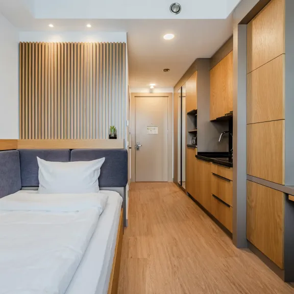 Modernes Einzelzimmer mit Holzboden, Bett, Schreibtisch und Fernseher an der Wand.