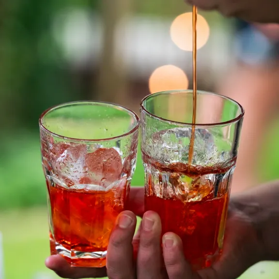 Zwei Gläser mit orangefarbenen Getränken und Eiswürfeln werden im Freien gehalten.