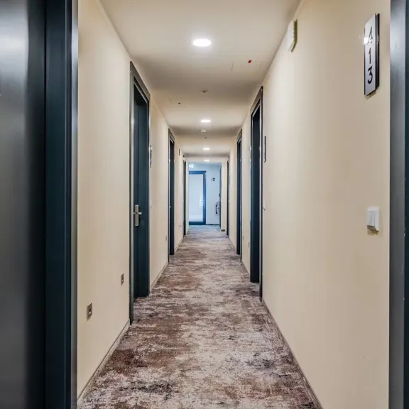 Heller Hotelflur mit blauen Türen und Teppichboden, Blickrichtung Ausgang.