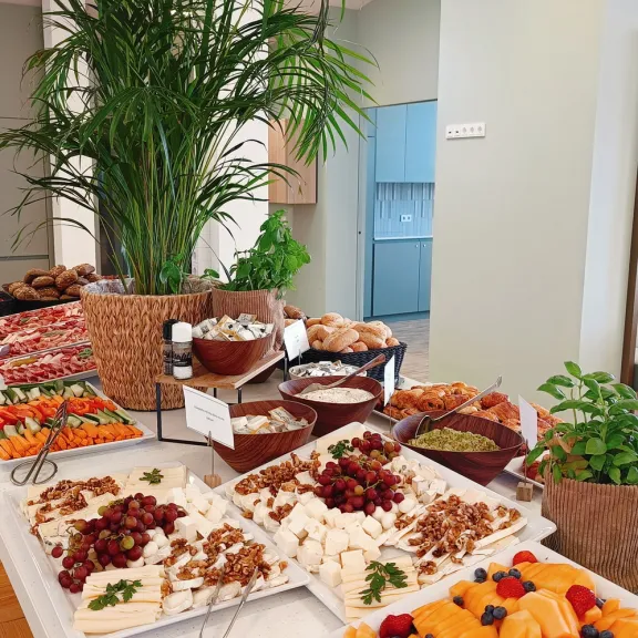 Buffet mit Obst, Gebäck und Nüssen, im Hintergrund grüne Pflanzen und helles Interieur.