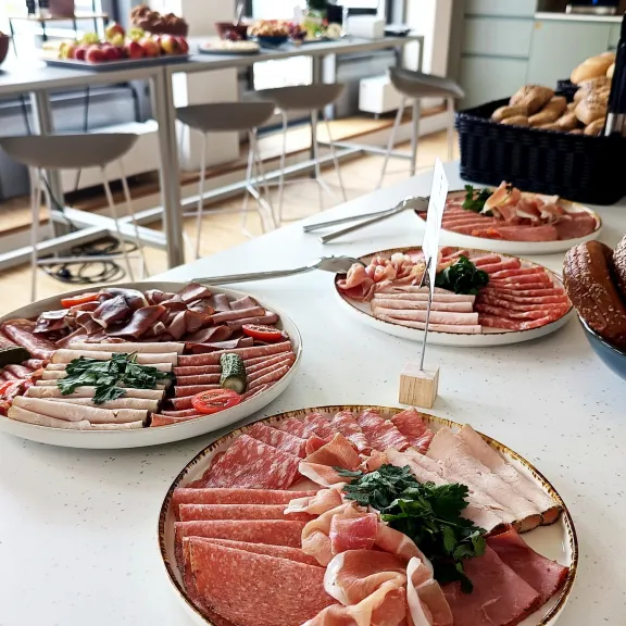 Auf einem Buffet stehen Teller mit verschiedenen Wurstsorten und Brot.