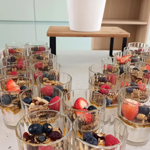 Joghurtgläser mit Müsli und Beeren auf einem Tisch, im Hintergrund Pflanze in weißem Topf.