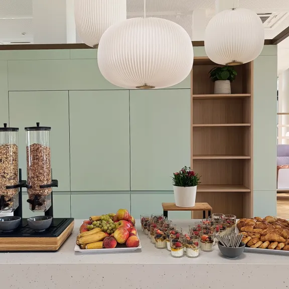 Frühstücksbuffet mit Müsli, Obst, Gebäck und großen runden Lampen darüber.