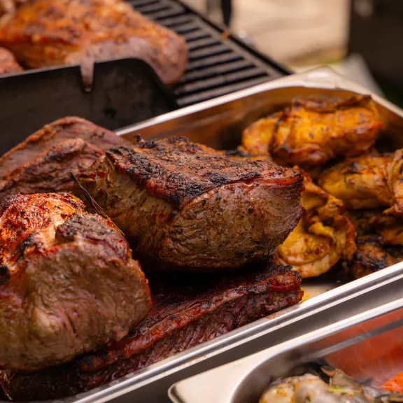 Gegrilltes Fleisch und Hähnchenteile auf einem Tablett neben einem Grill.