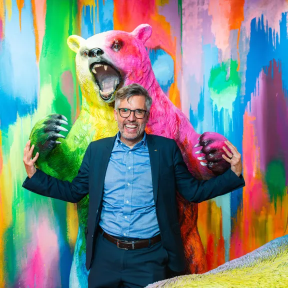 Mann vor farbigem Bärenkunstwerk, beide mit erhobenen Armen und fröhlichem Gesicht.