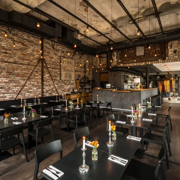 Modernes Restaurant mit Backsteinwand, gedeckten Tischen und Kerzen, industrielle Einrichtung.
