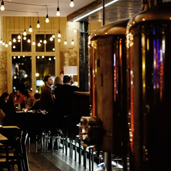 Gemütliches Restaurant mit Lichterketten und großen Kupfertanks im Vordergrund.