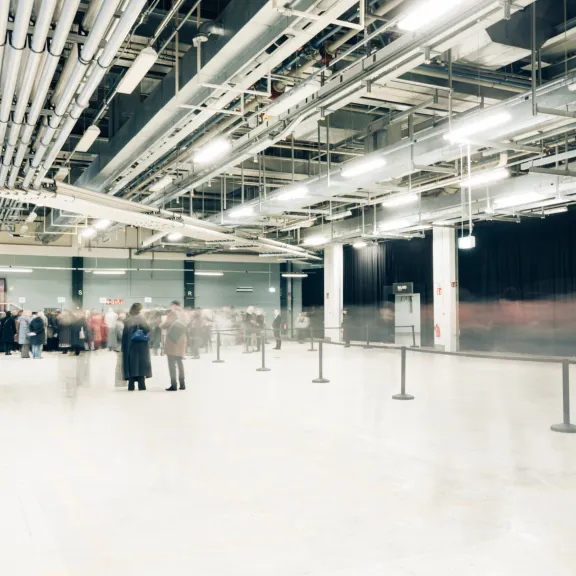 Große helle Halle mit Menschenansammlung im Hintergrund, viele Rohre an der Decke