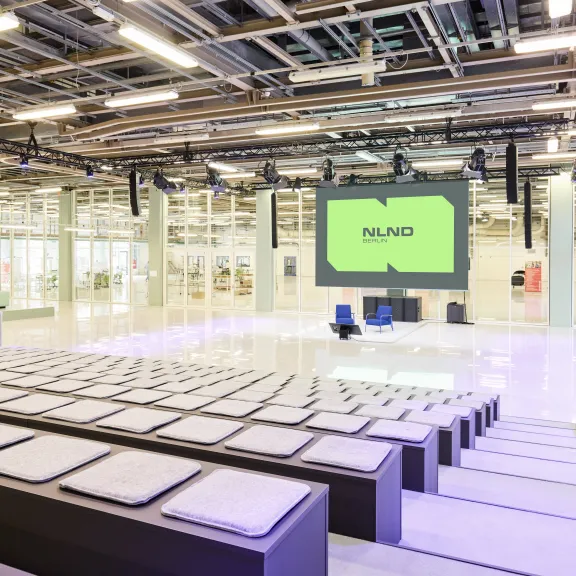 Heller, moderner Konferenzsaal mit großen Sitzstufen und einer Bühne samt Leinwand.