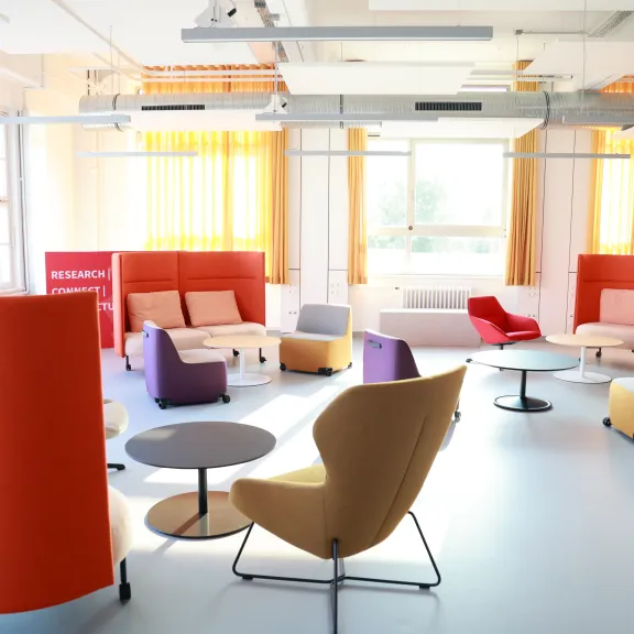 Heller Aufenthaltsraum mit bunten Sesseln, Sofas und runden Tischen.