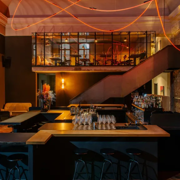 Moderne Bar mit dunkler Einrichtung, leeren Hockern und roten Lichtlinien an der Decke.