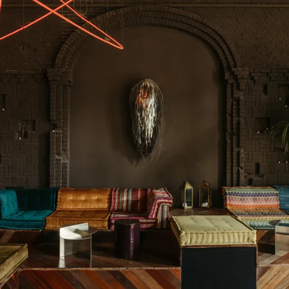 Bunte Sofas und Tische vor dunkelbrauner Wand mit Kunstwerk, warme gemütliche Atmosphäre.