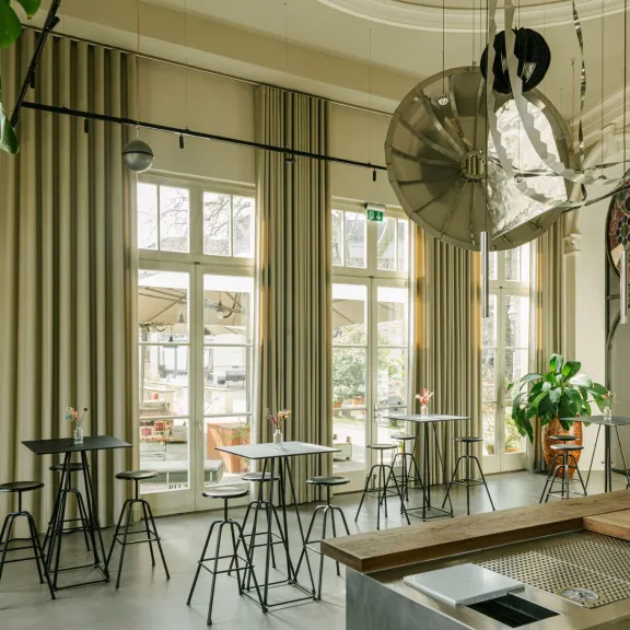 Helles Café mit großen Fenstern, Pflanzen und modernen Holzmöbeln