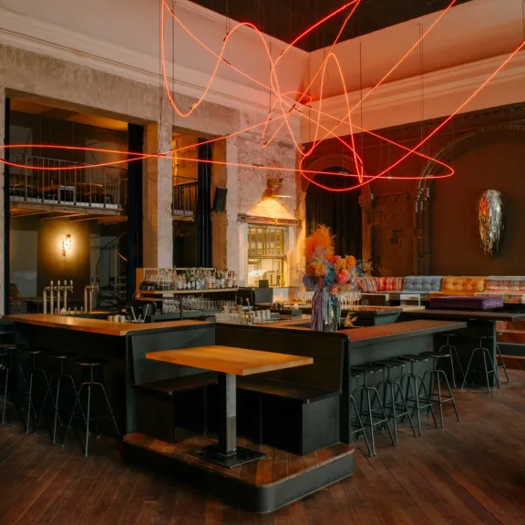 Modernes Restaurant mit Holzboden, bunter Einrichtung und leuchtender roter Lichtinstallation.