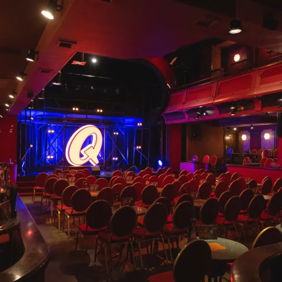 Roter Theatersaal mit runden Tischen, Bühne und beleuchtetem Q im Hintergrund