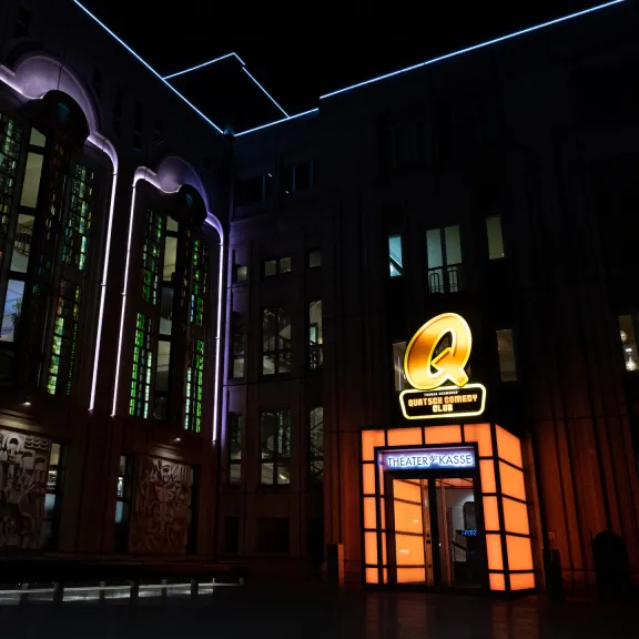 Beleuchtetes Gebäude bei Nacht mit bunten Lichtern und einem leuchtenden Logo über dem Eingang.