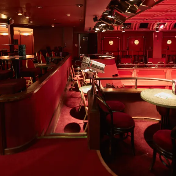 Roter, leerer Theater- oder Nachtclubraum mit Tischen und gepolsterten Stühlen.