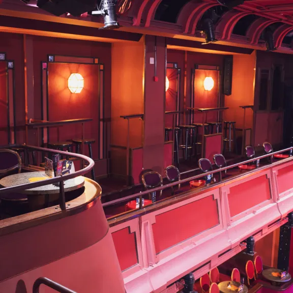 Roter Theatersaal mit Balkon, leeren Stühlen und warmem Licht