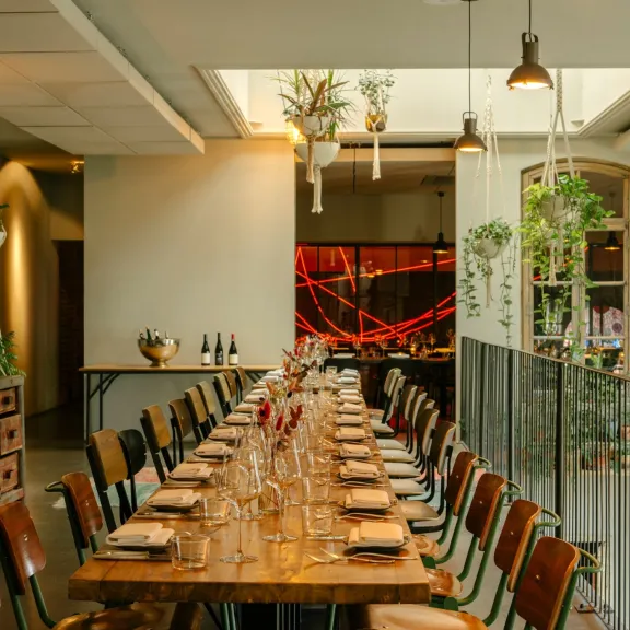 Langer, festlich gedeckter Tisch in modernem Restaurant mit Pflanzen und warmem Licht.