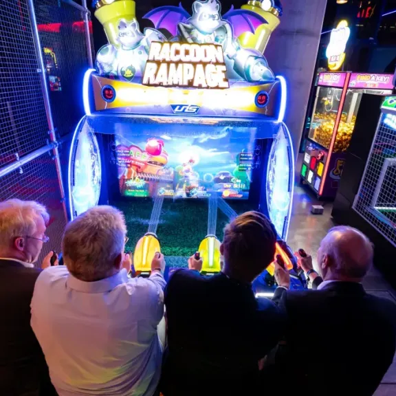 Vier Männer spielen zusammen ein buntes Arcade-Spiel in einer Spielhalle.