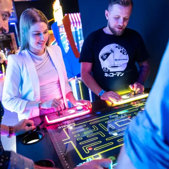 Vier Personen spielen gemeinsam an einem bunten Pac-Man Arcade-Automaten.