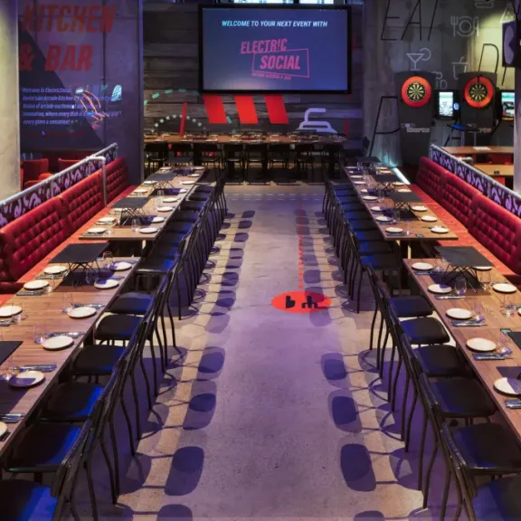 Modernes Restaurant mit langen Holztischen, roten Polsterbänken und dunklem Ambiente.