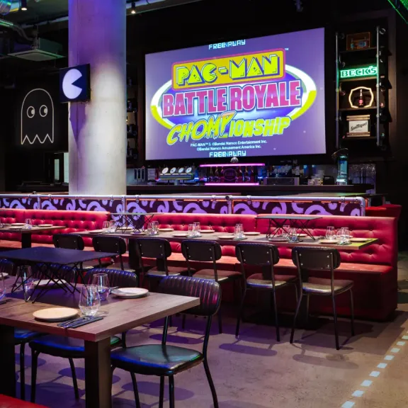 Modernes Restaurant mit roten Sitzbänken und großem Pac-Man-Spiele-Screen an der Wand.