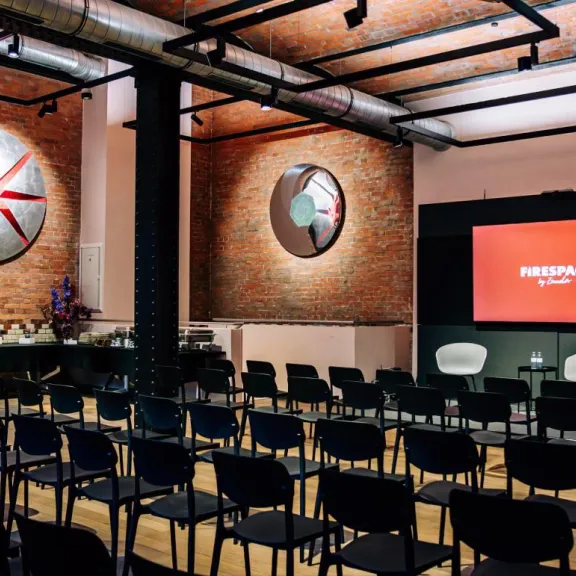 Tagung mit Reihenbestuhlung, Panel-Bühne und LED-Display unter 6 m hohen Decken im Firespace