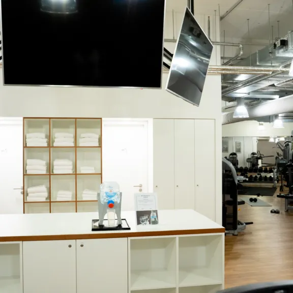 Heller Fitnessstudio-Empfang mit Handtüchern und Wasserspender, Geräte im Hintergrund