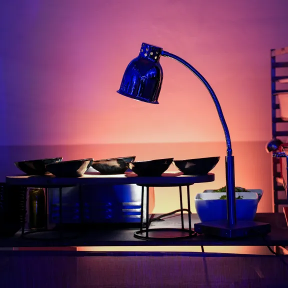 Buffet mit schwarzen Schalen unter einer warmen Lampe, bunte Beleuchtung im Hintergrund.