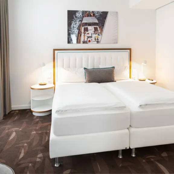 Modernes Hotelzimmer mit zwei weißen Einzelbetten, Nachttischen und Wandbild.