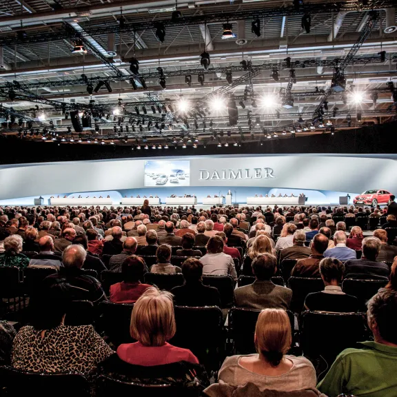 Großer Konferenzsaal mit vielen sitzenden Menschen vor einer beleuchteten Bühne.