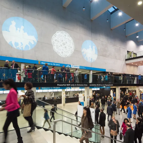 Viele Menschen in einer modernen Messehalle mit Projektionen an der Wand.