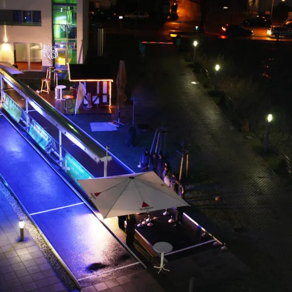 Beleuchtete Terrasse mit Sonnenschirmen und blau-violettem Licht bei Nacht