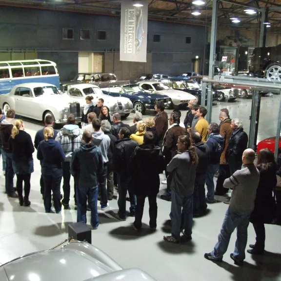 Gruppe Menschen in einer Oldtimerausstellung, umgeben von klassischen Autos.