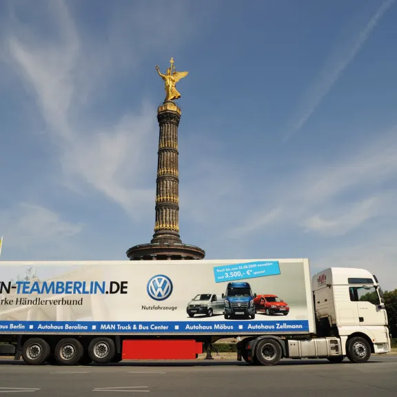 LKW vor der Berliner Siegessäule bei blauem Himmel, Werbeaufschrift am LKW.