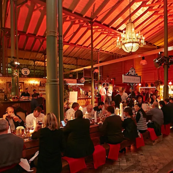 Volles Restaurant mit roten Lichtern, großen Kronleuchtern und langen Holztischen.