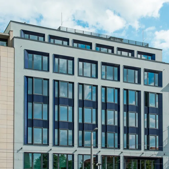 Modernes sechsstöckiges Bürogebäude mit großen Fenstern und Glasfassade bei Tag.