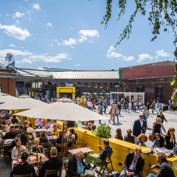 Menschen genießen sonniges Wetter unter Sonnenschirmen auf einem belebten Platz