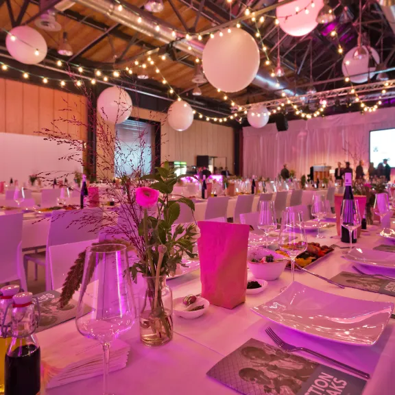 Festlich gedeckter Saal mit langen Tischen, warmem Licht und hängenden Dekokugeln