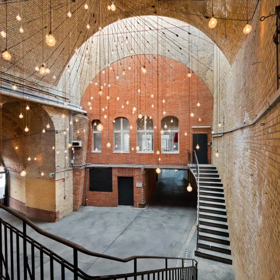 Großer Backsteinraum mit Gewölbedecke, Hängelampen und breiter Treppe.