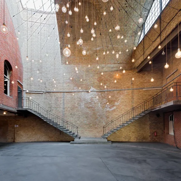 Innenhof mit Backsteinwänden, Treppen und vielen hängenden Glühbirnen