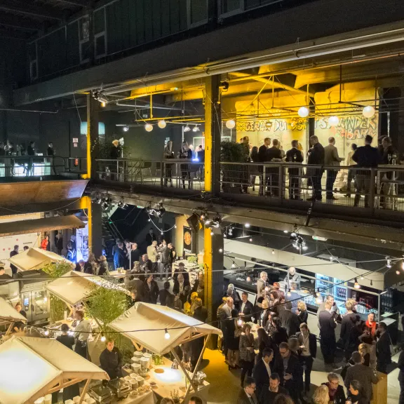 Menschen bei einer Veranstaltung in einer modernen, zweistöckigen Halle mit hellem Licht.