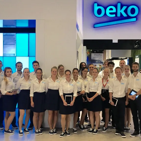 Gruppe von Mitarbeitern in einheitlicher Kleidung vor einem beko-Stand auf einer Messe.