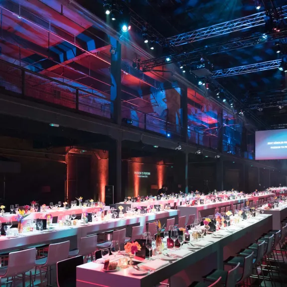 Festlich gedeckter Saal mit langen Tischen und stimmungsvoller Beleuchtung.