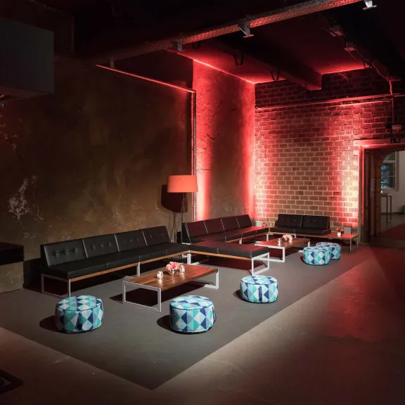 Lounge-Bereich mit Sofas, roten Lichtern und bunten Sitzhockern in modernem Raum.