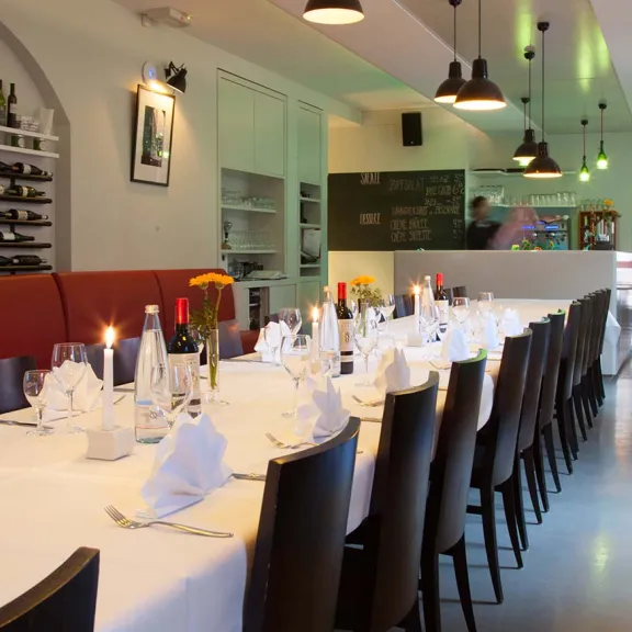 Langer, festlich gedeckter Tisch in modernem Restaurant mit Kerzen und Weingläsern.