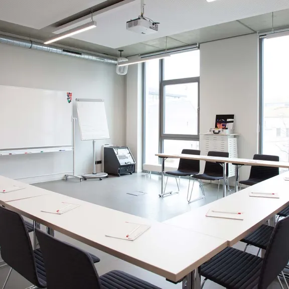 Heller Konferenzraum mit U-förmigem Tisch, Stühlen und Whiteboard.